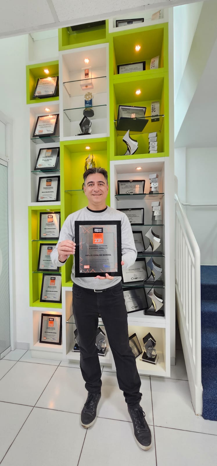 Leonardo Paixão diante da estante de troféus e selos conquistados pela inFlux English School